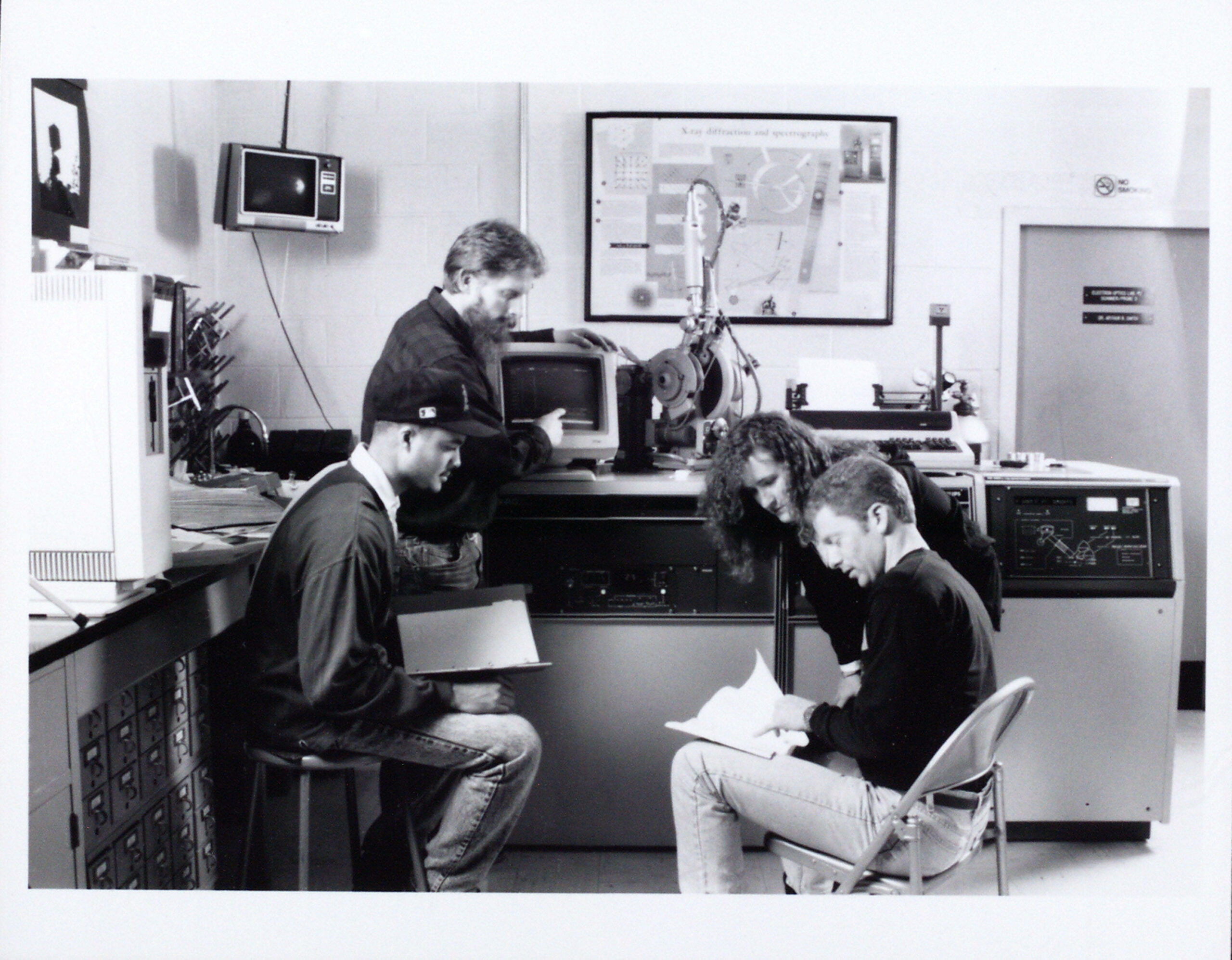 Black and white photo of West Chester University students huddled around new computer.